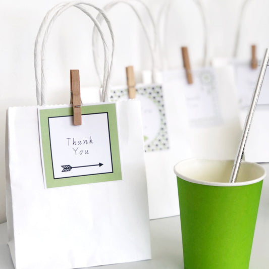 Green and black editable square labels on a party table set up on white background. There is a green cup in the foreground. 