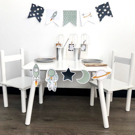 Space themed Party Decorations set up on white table with bunting flags and cut out shapes. 