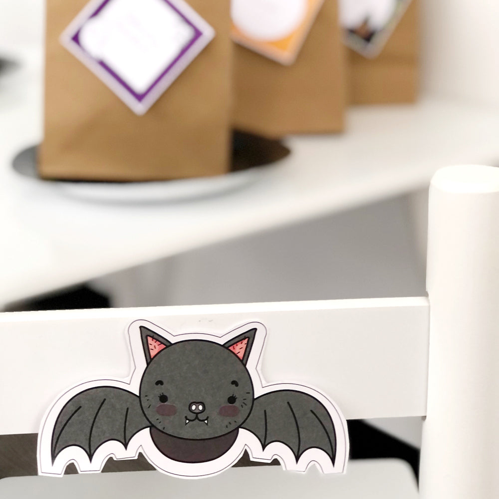 Cute black Halloween Bat printable displayed on white chair as a party table set up decoration.