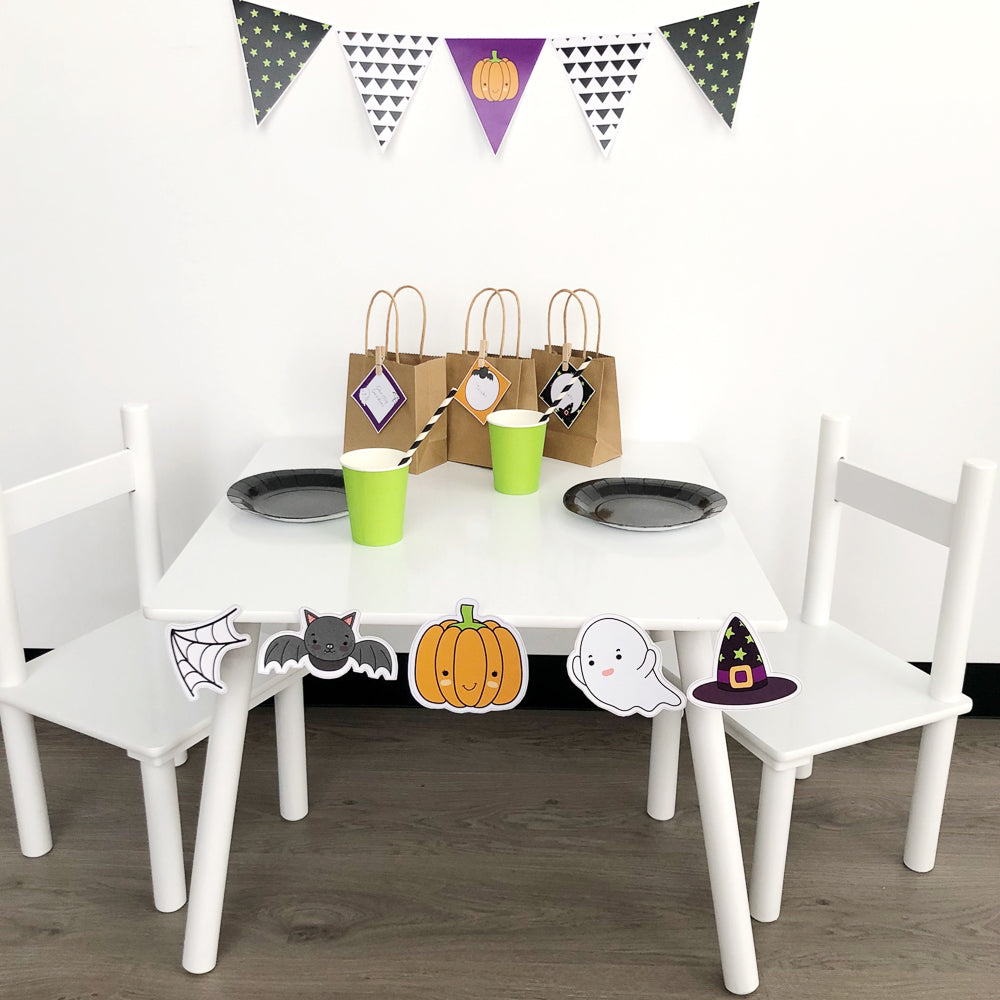 Halloween themed kids party set up on white table. Features pumpkin, bat, spider web and ghost. 