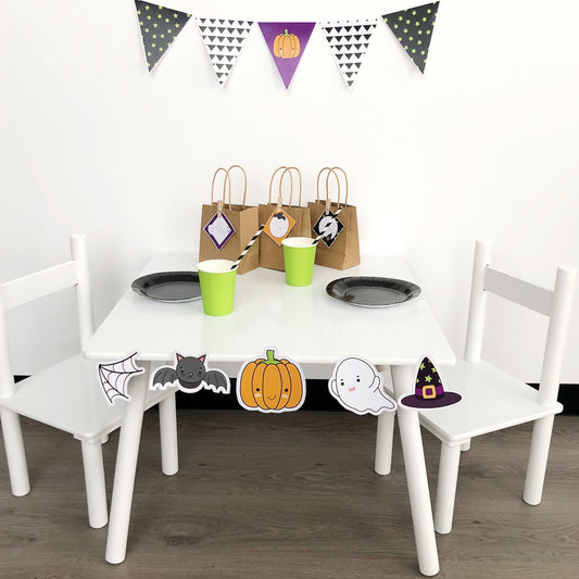 Halloween themed kids party set up on white table. Features pumpkin, bat, spider web and ghost. 