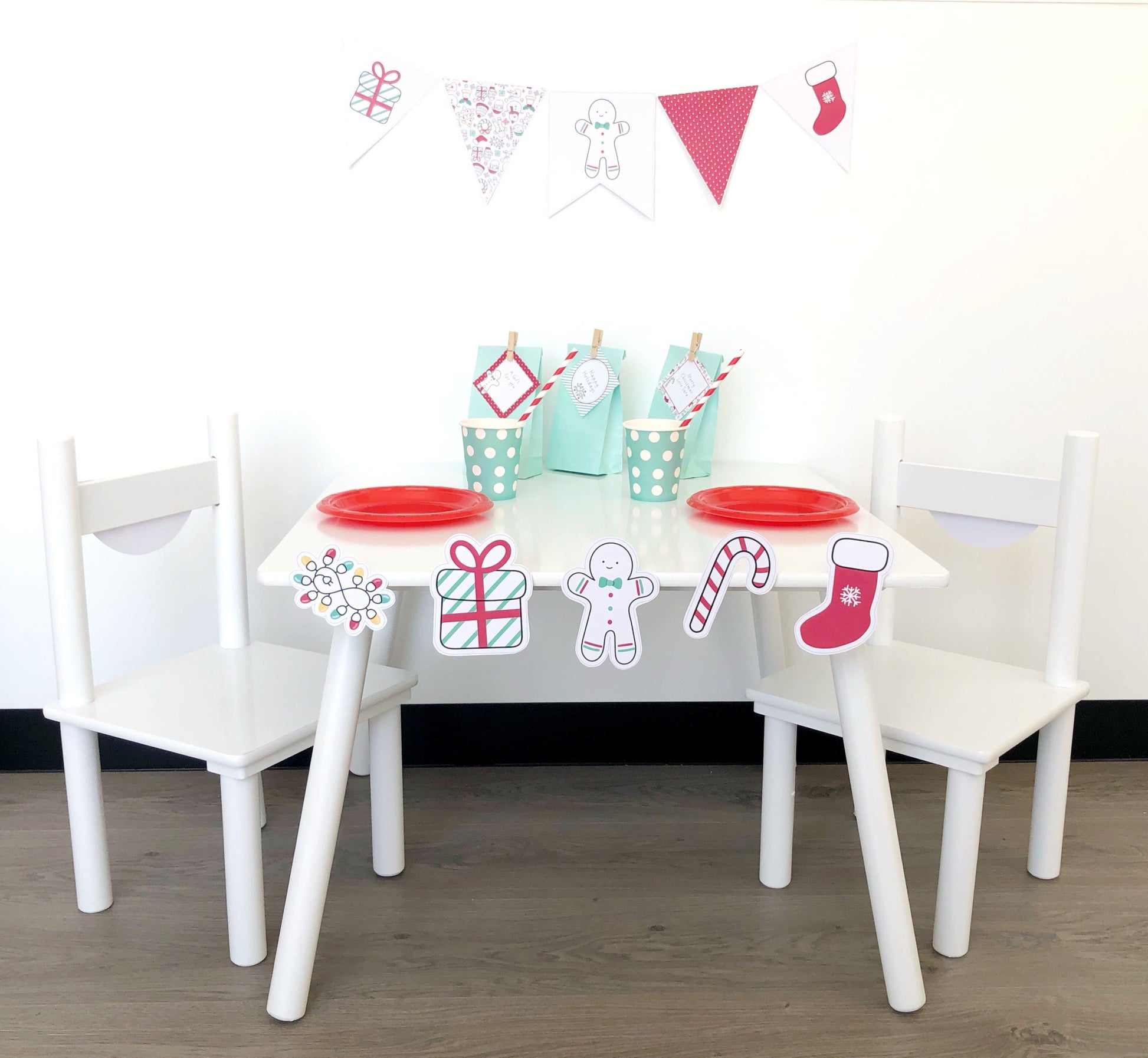 A set of three white chairs with a Christmas-themed decoration pack, including bunting, flags, and gingerbread man cutouts, with a table in the middle.