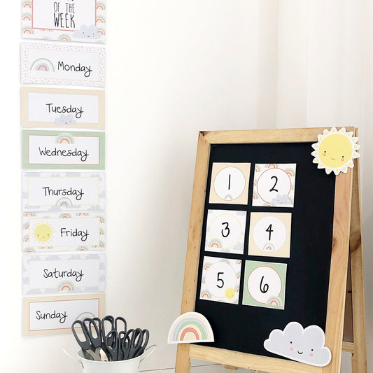 Pastel rainbow themed classroom decor signs on a blackboard and white wall. 