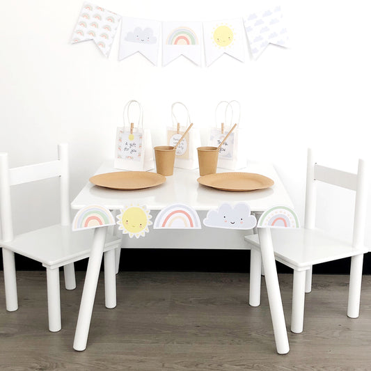 Pastel rainbow theme party set up with white table and chairs and bunting flags on the wall. 