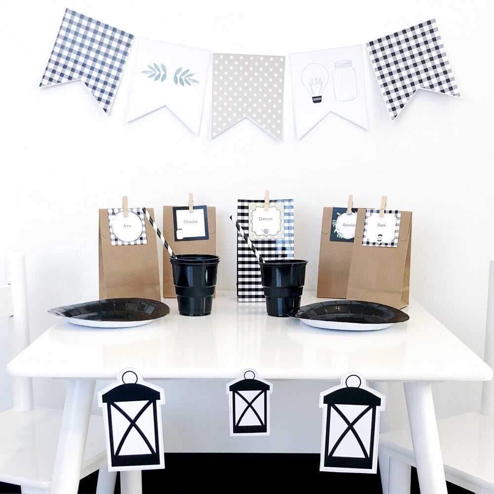 Black and White farmhouse theme party table with party bags, bunting flag, plates and cups. Lantern shapes are placed on the white table. 