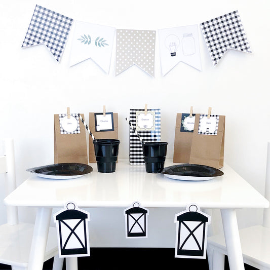 Black and White farmhouse theme party table with party bags, bunting flag, plates and cups. Lantern shapes are placed on the white table. 