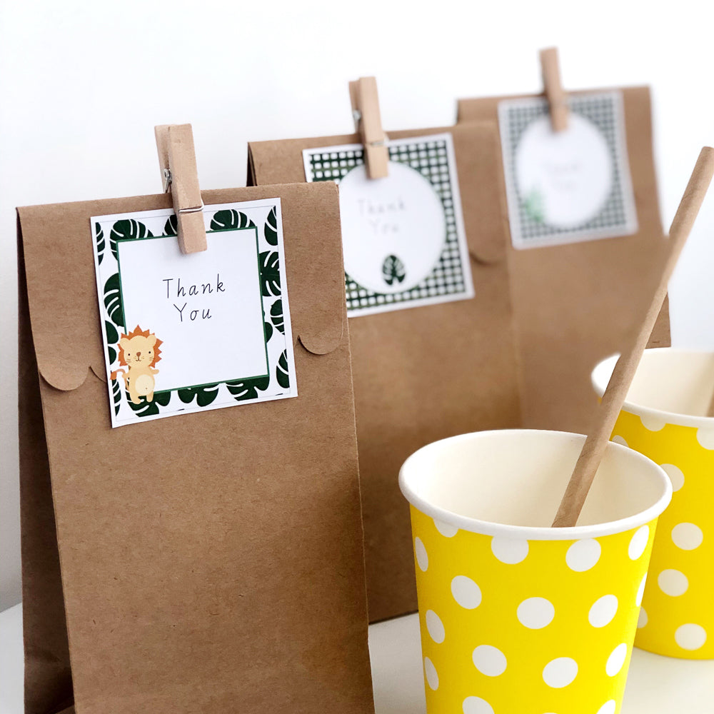 Brown party bags with jungle safari theme gift tags behind yellow cups on a white table. 