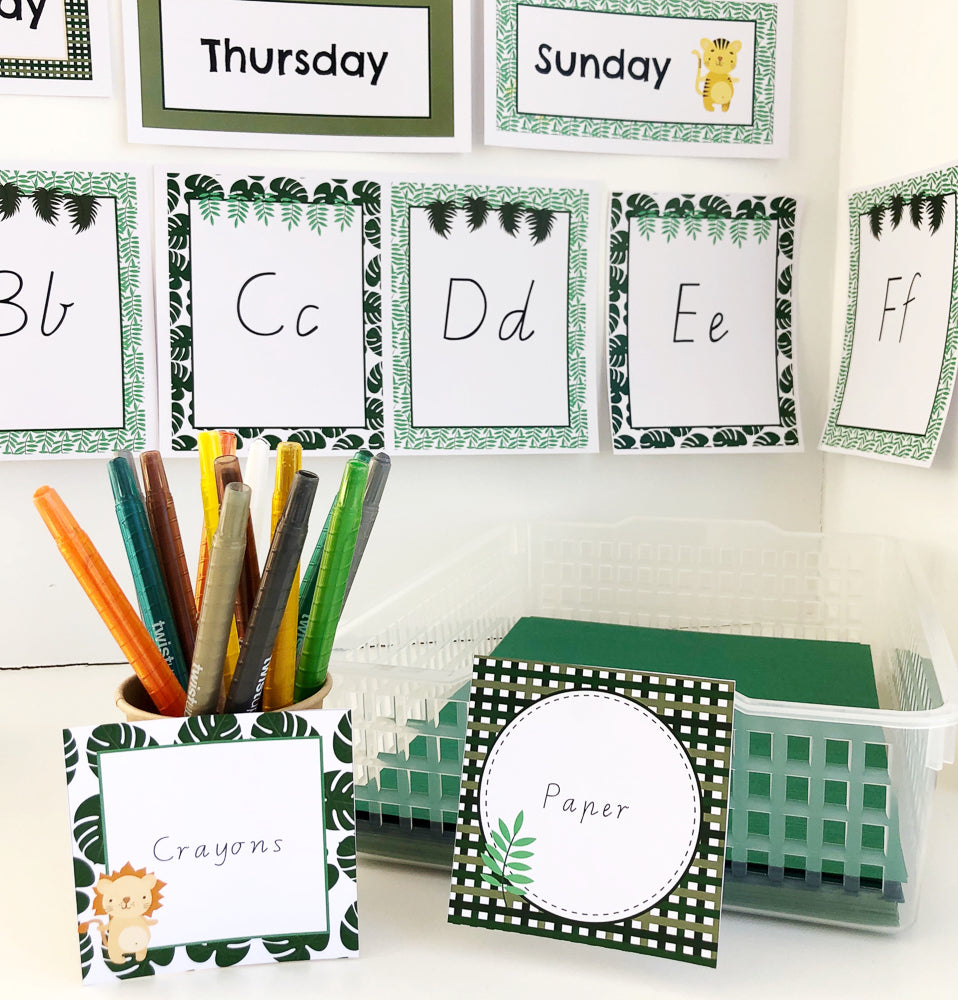 Safari jungle theme classroom decor displayed on white wall with  crayons and paper in front with square labels naming the items. 