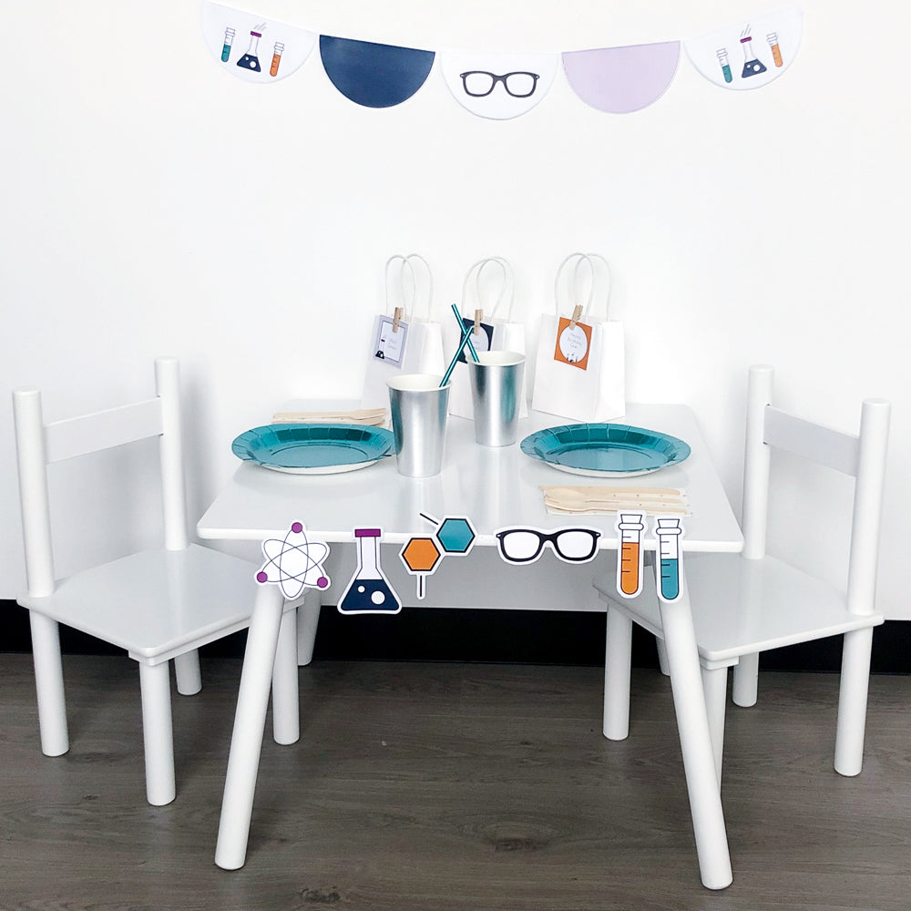 Science theme party table set up with plates, cups, scalloped bunting, party bags and cut out shapes. 