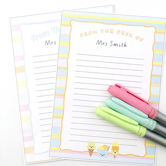 Two sheets of note paper with ice cream illustrations next to pastel markers on white background. 